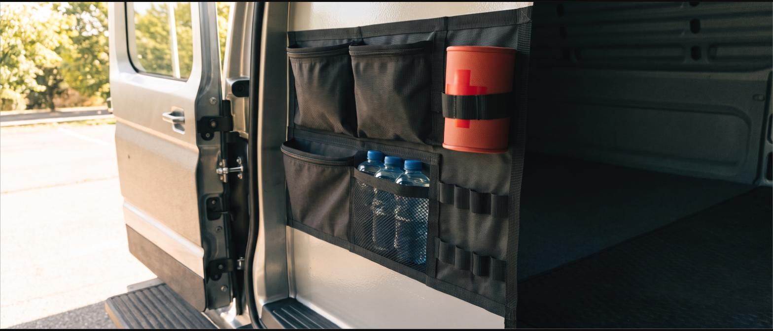 A webbing organizer panel mounted inside a van holding pouches, a first aid kit and water